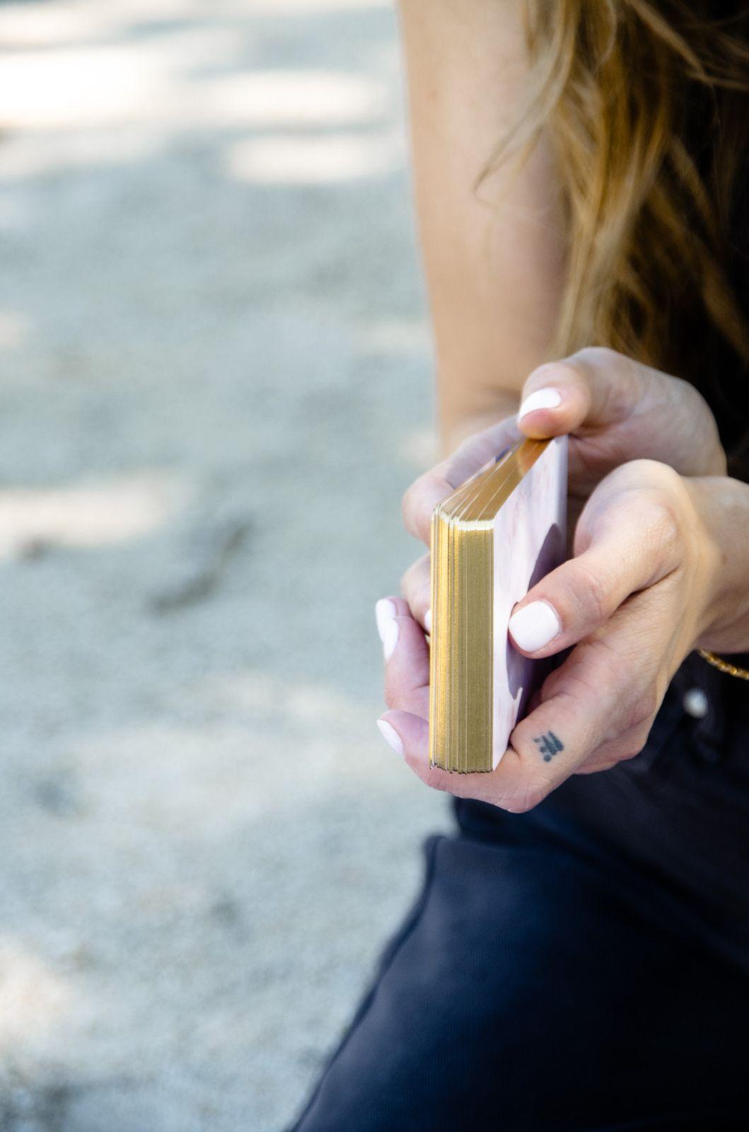 Anke's hands holding the deck, the gold edges of the cards catching the light