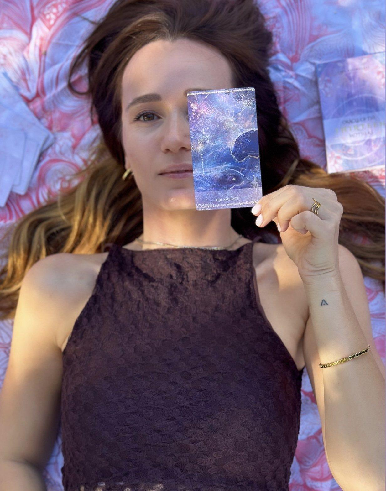 Anke lying on a mandala cloth, holding the Dreamspace card over half of her face