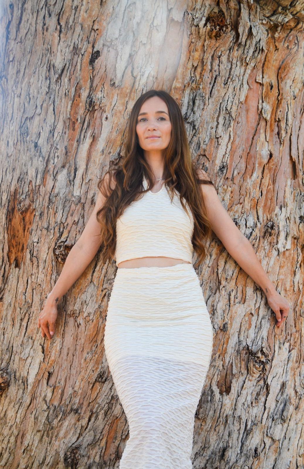 Anke in white against an old tree, looking straight into the camera